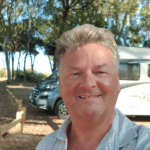 Foto vom Autor im Vordergrund, im Hintergrund sieht man das Wohnmobil vom Autor mit Küstenwald und Meer. Autor genießt das Leben im Wohnmobil.