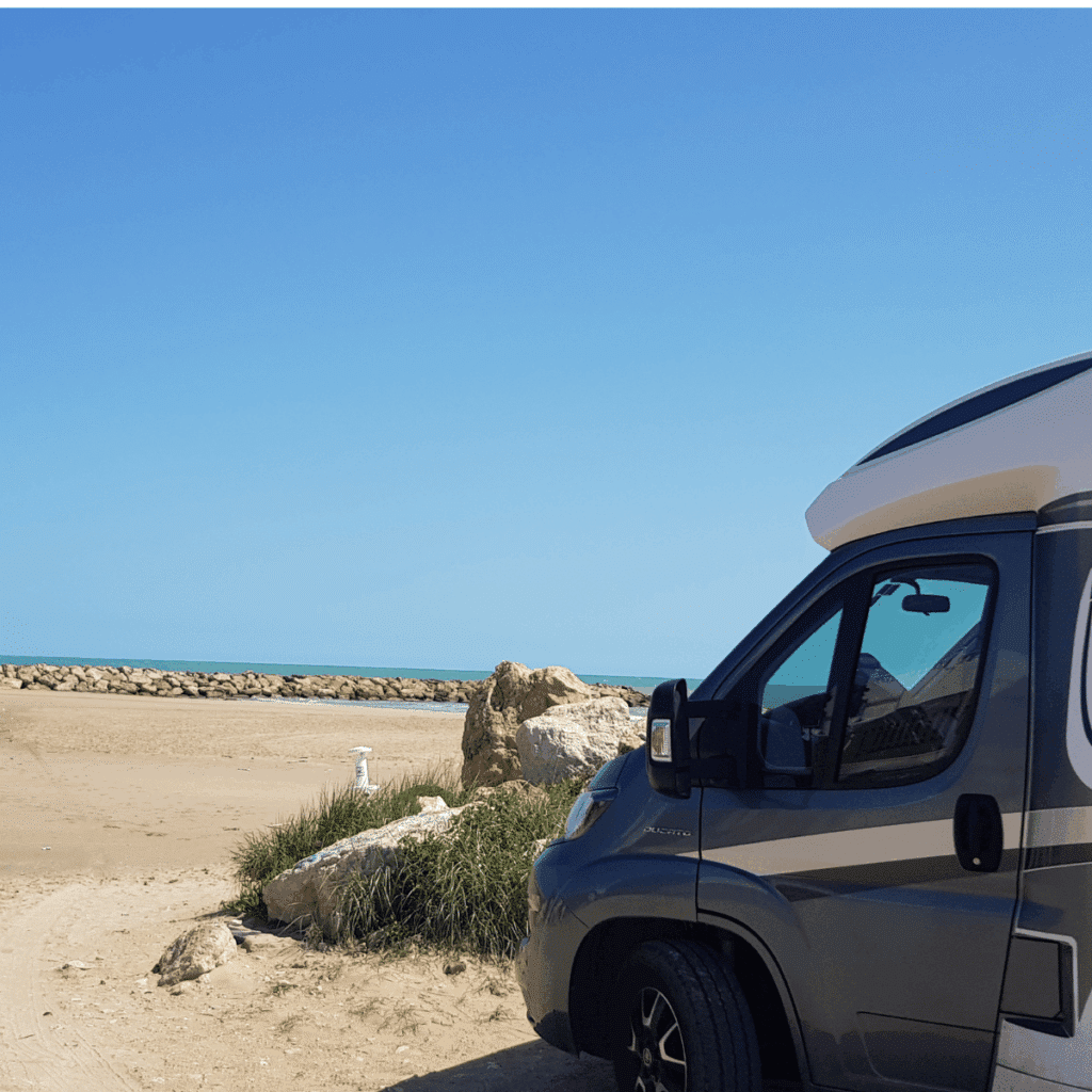 Das aktuelle Wohnmobil von Torsten Friedrich (Autor) am Mittelmeerstrand vor einer Steinpackung der Bunen, am Horizont türkisfarbenes Mittelmeer zu sehen.